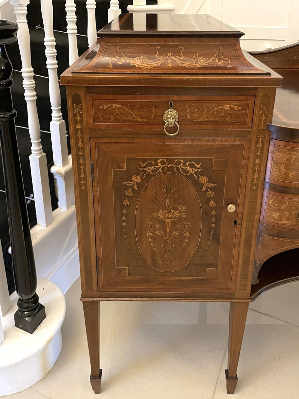 A nineteenth-century mahogany sideboard with detailed floral marquetry inlays, a stepped pedestal top, multiple drawers with brass lion mask ring handles, and tapered square legs. View VIII