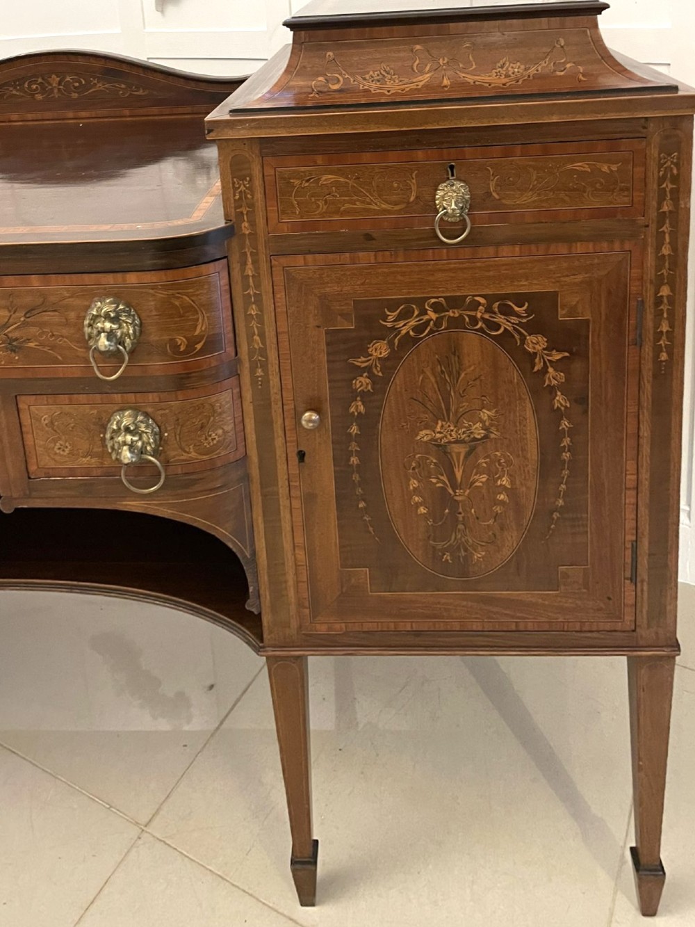 A nineteenth-century mahogany sideboard with detailed floral marquetry inlays, a stepped pedestal top, multiple drawers with brass lion mask ring handles, and tapered square legs. View X