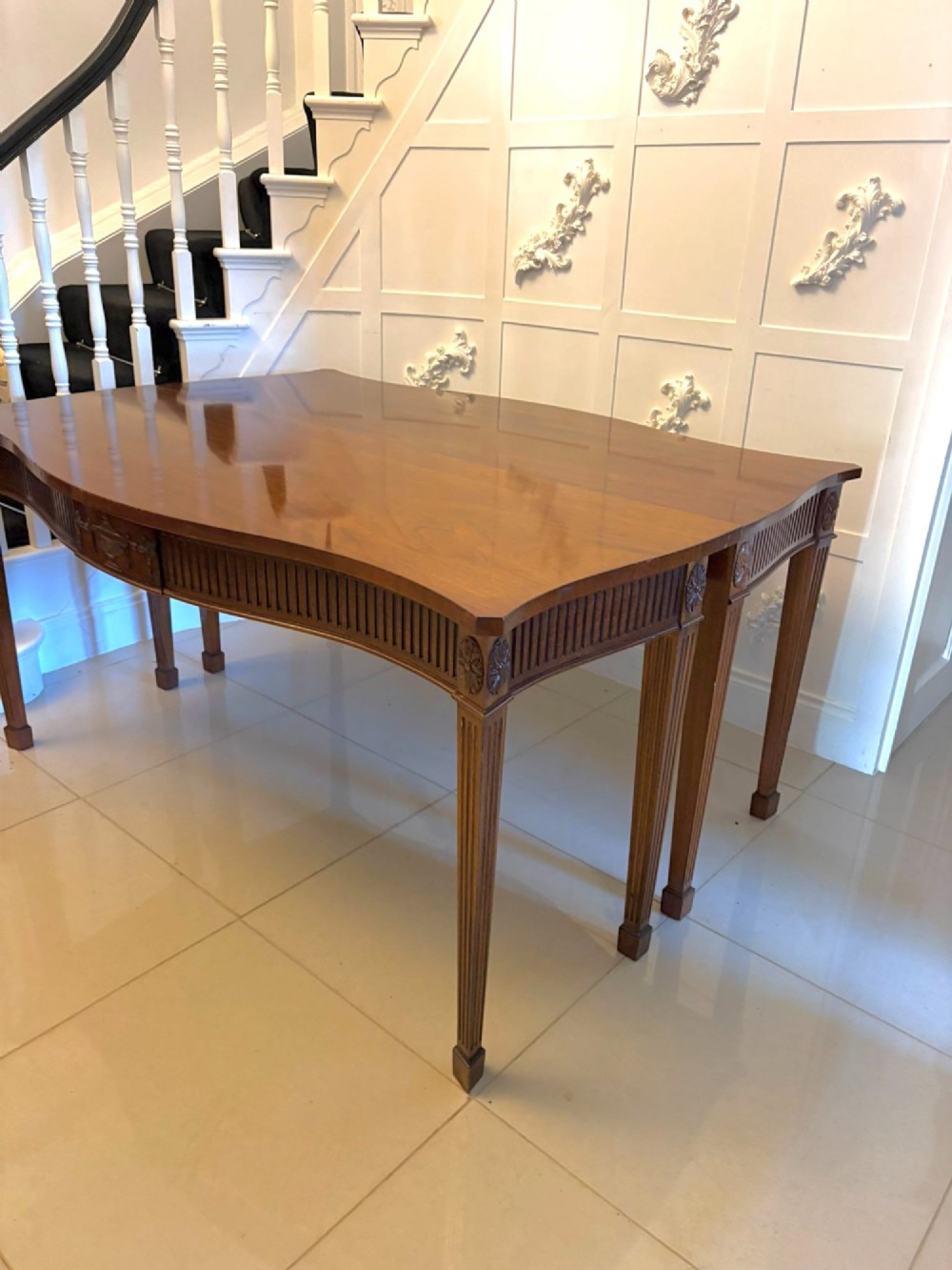 A pair of polished mahogany serpentine-front console tables featuring fluted aprons, carved central urn motifs, and tapered fluted legs. View V