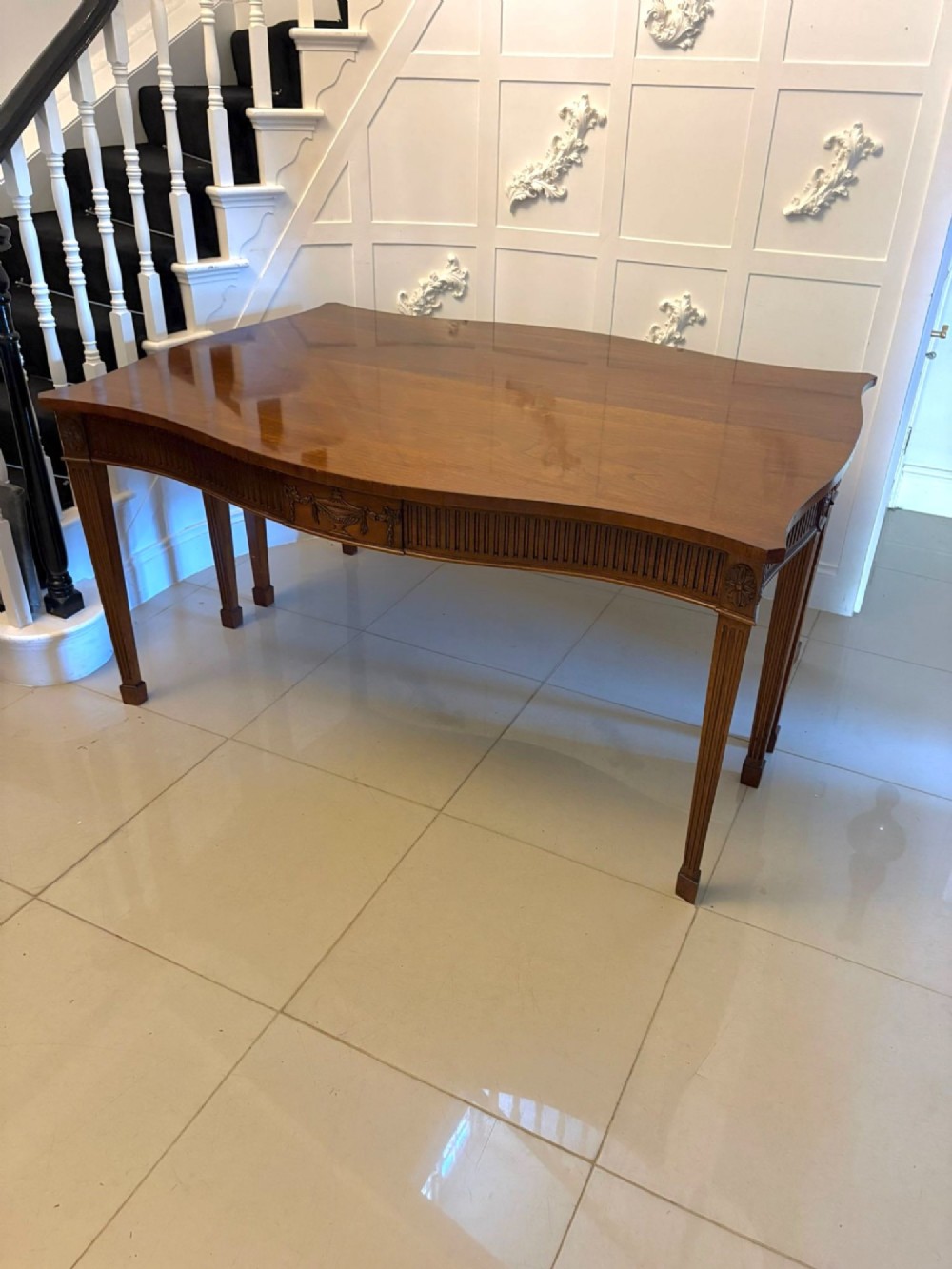 A pair of polished mahogany serpentine-front console tables featuring fluted aprons, carved central urn motifs, and tapered fluted legs. View VI
