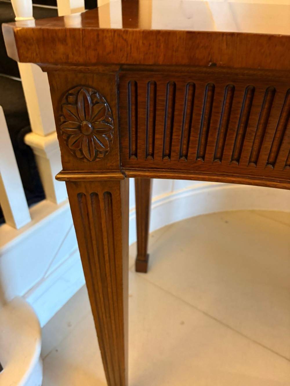 A pair of polished mahogany serpentine-front console tables featuring fluted aprons, carved central urn motifs, and tapered fluted legs. View VIII