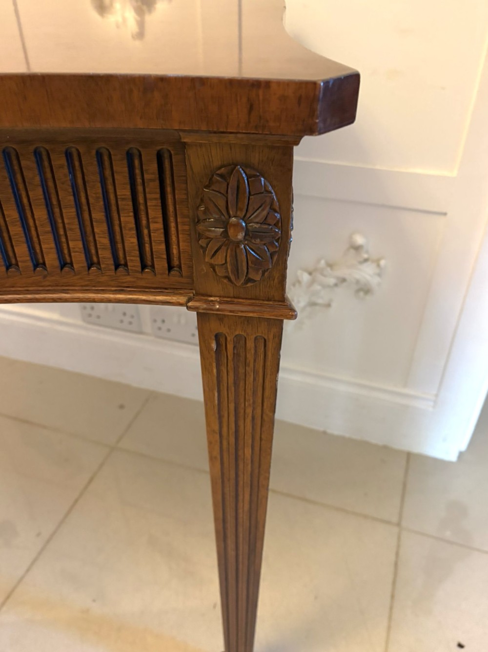 A pair of polished mahogany serpentine-front console tables featuring fluted aprons, carved central urn motifs, and tapered fluted legs. View X