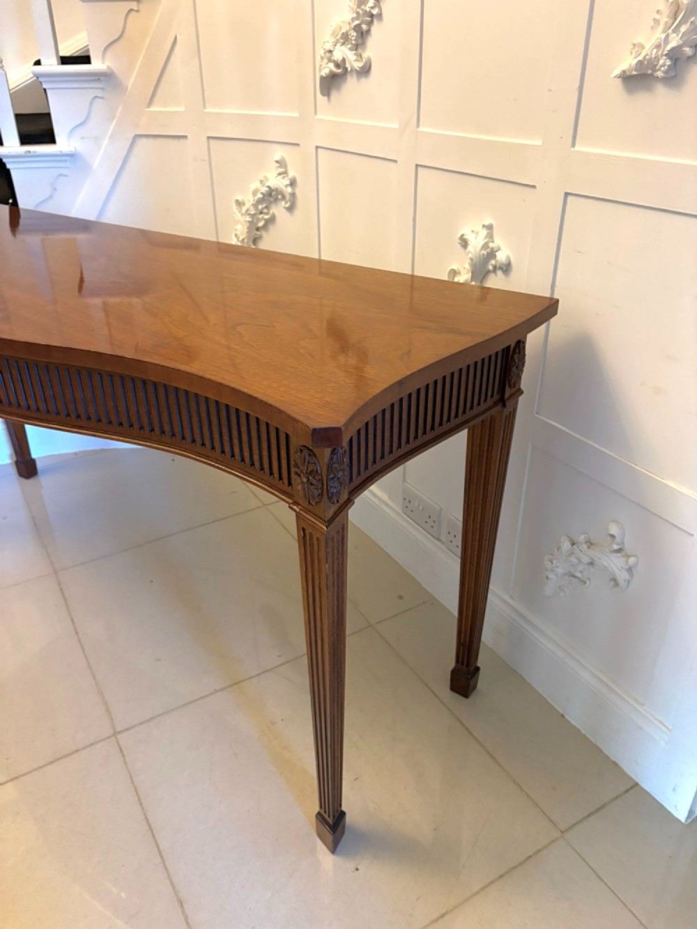 A pair of polished mahogany serpentine-front console tables featuring fluted aprons, carved central urn motifs, and tapered fluted legs. View XI