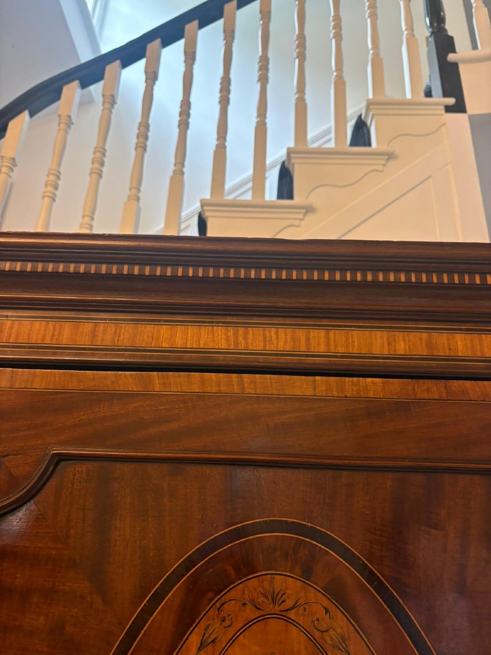 An antique Georgian mahogany linen press featuring two doors decorated with oval satinwood urn marquetry inlays situated above four drawers with brass handles. View VI