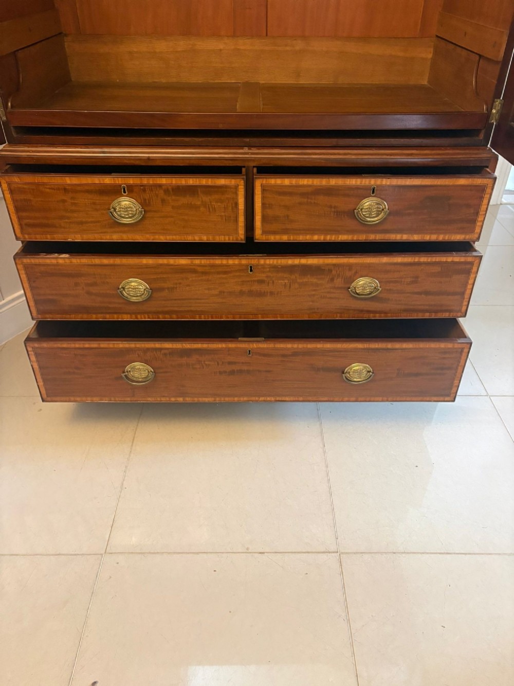 An antique Georgian mahogany linen press featuring two doors decorated with oval satinwood urn marquetry inlays situated above four drawers with brass handles. View VIII