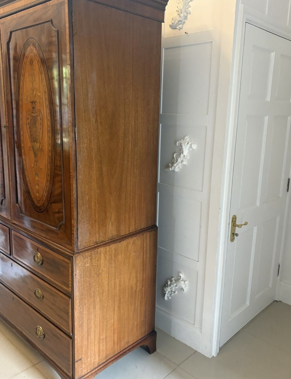 An antique Georgian mahogany linen press featuring two doors decorated with oval satinwood urn marquetry inlays situated above four drawers with brass handles. View IX