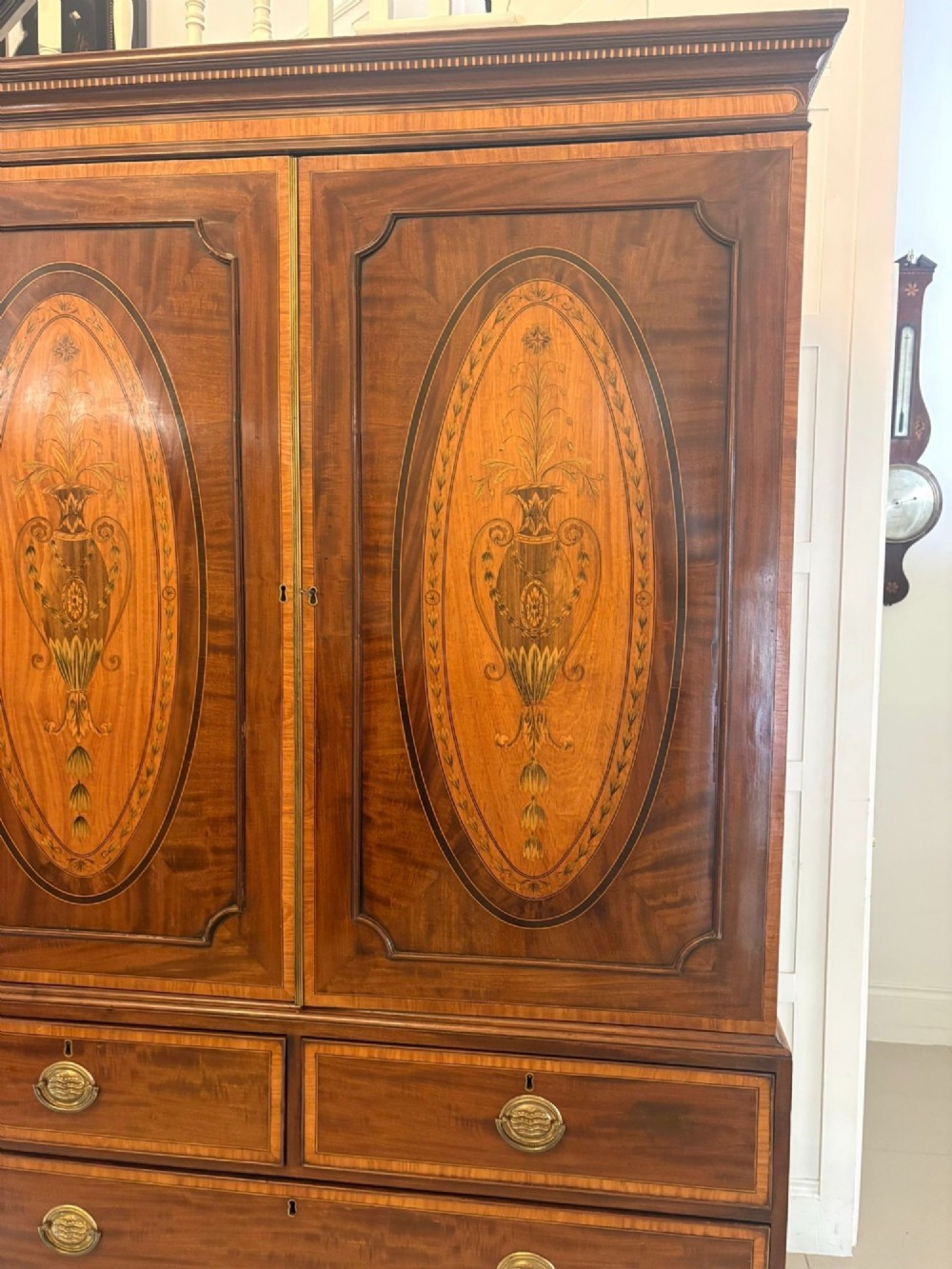 An antique Georgian mahogany linen press featuring two doors decorated with oval satinwood urn marquetry inlays situated above four drawers with brass handles. View X