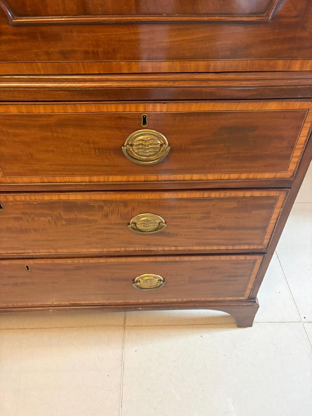 An antique Georgian mahogany linen press featuring two doors decorated with oval satinwood urn marquetry inlays situated above four drawers with brass handles. View XI