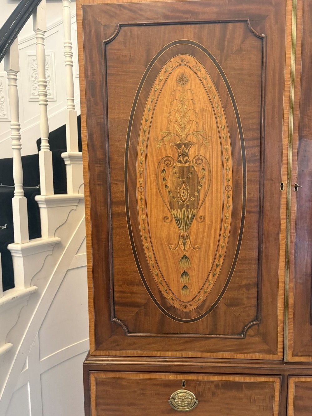 An antique Georgian mahogany linen press featuring two doors decorated with oval satinwood urn marquetry inlays situated above four drawers with brass handles. View XIII