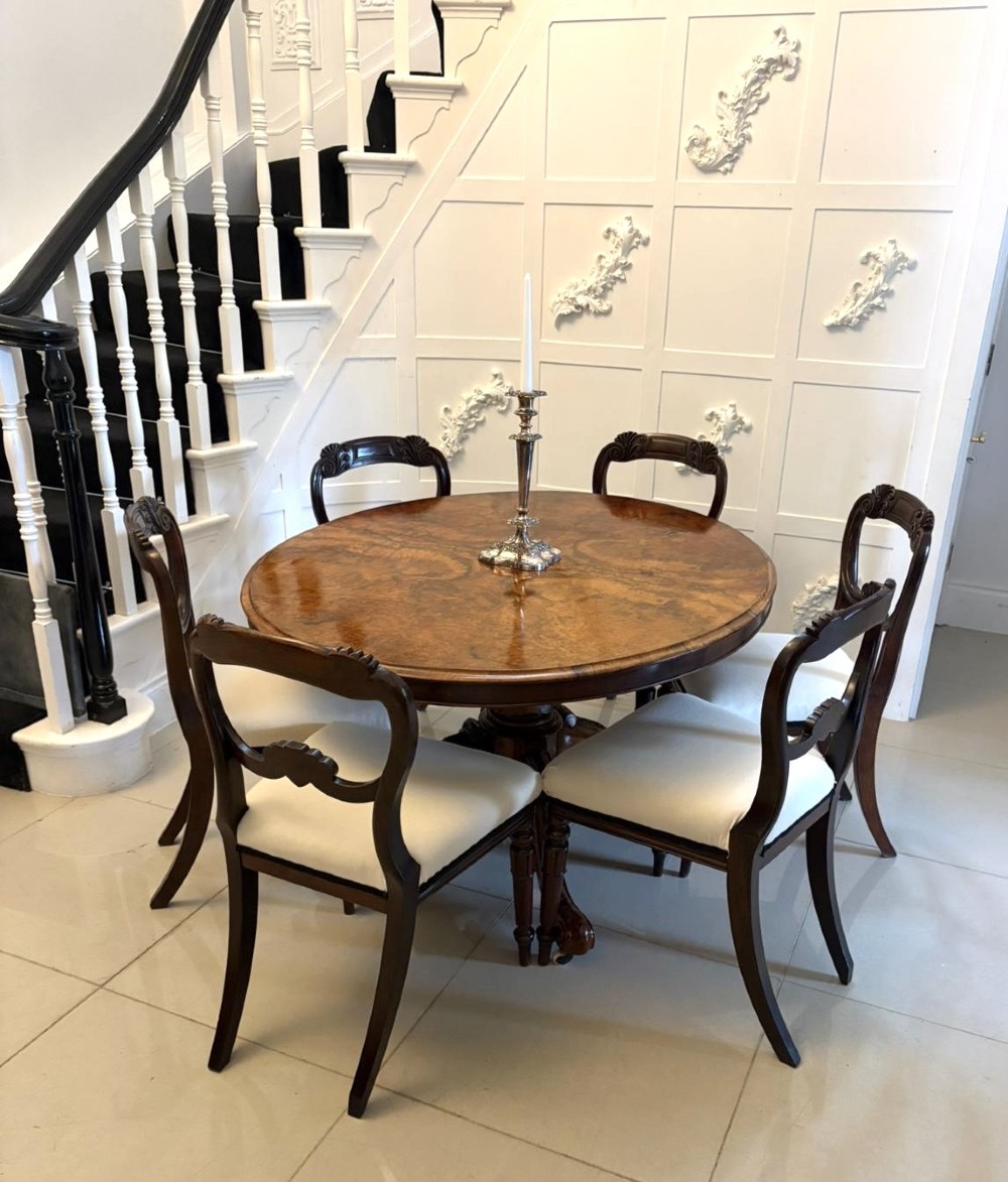 An antique Victorian oval tilt-top dining table featuring book-matched burr walnut grain mounted on a carved central column and tripod base with castors. View V