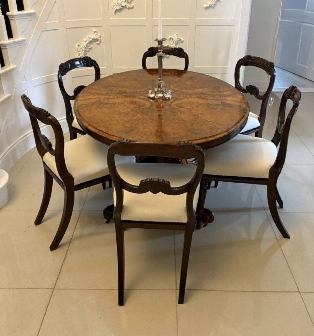 An antique Victorian oval tilt-top dining table featuring book-matched burr walnut grain mounted on a carved central column and tripod base with castors. View VI