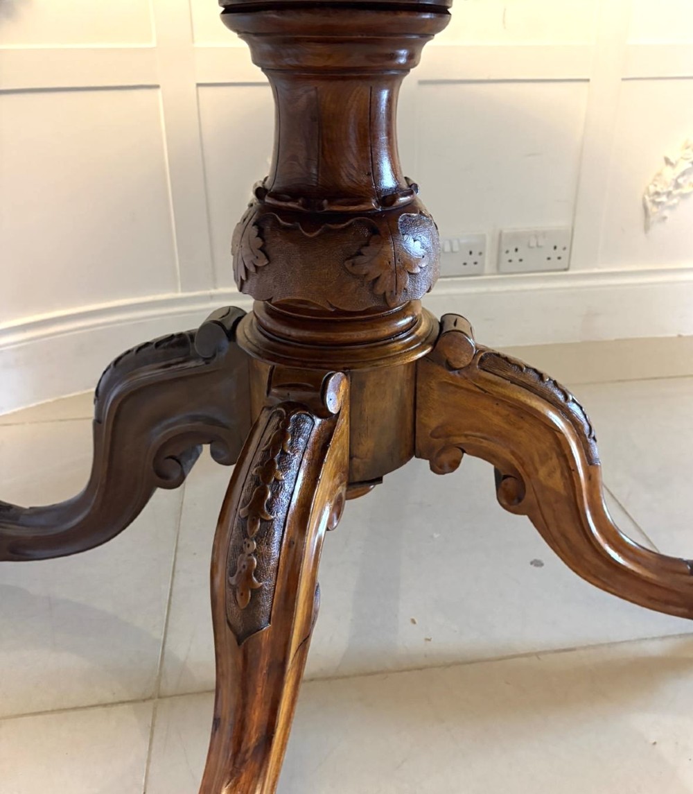 An antique Victorian oval tilt-top dining table featuring book-matched burr walnut grain mounted on a carved central column and tripod base with castors. View X
