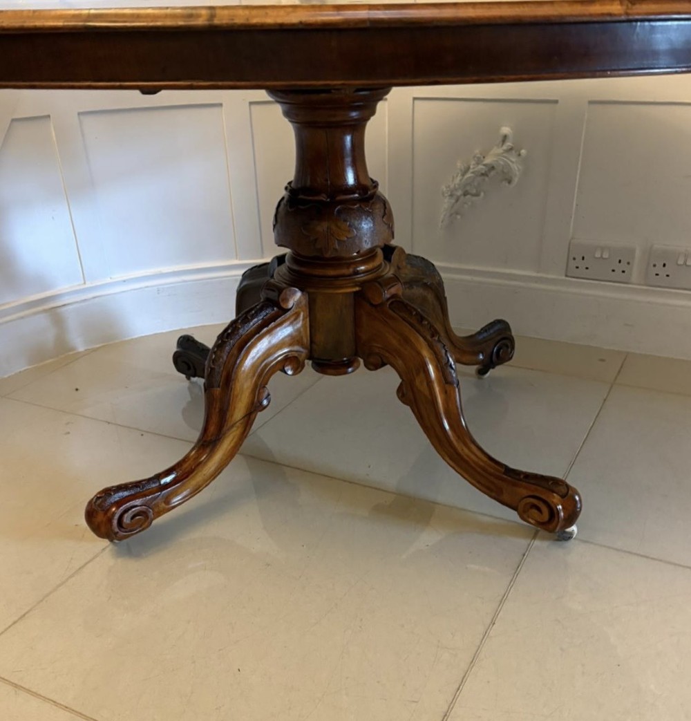 An antique Victorian oval tilt-top dining table featuring book-matched burr walnut grain mounted on a carved central column and tripod base with castors. View XII