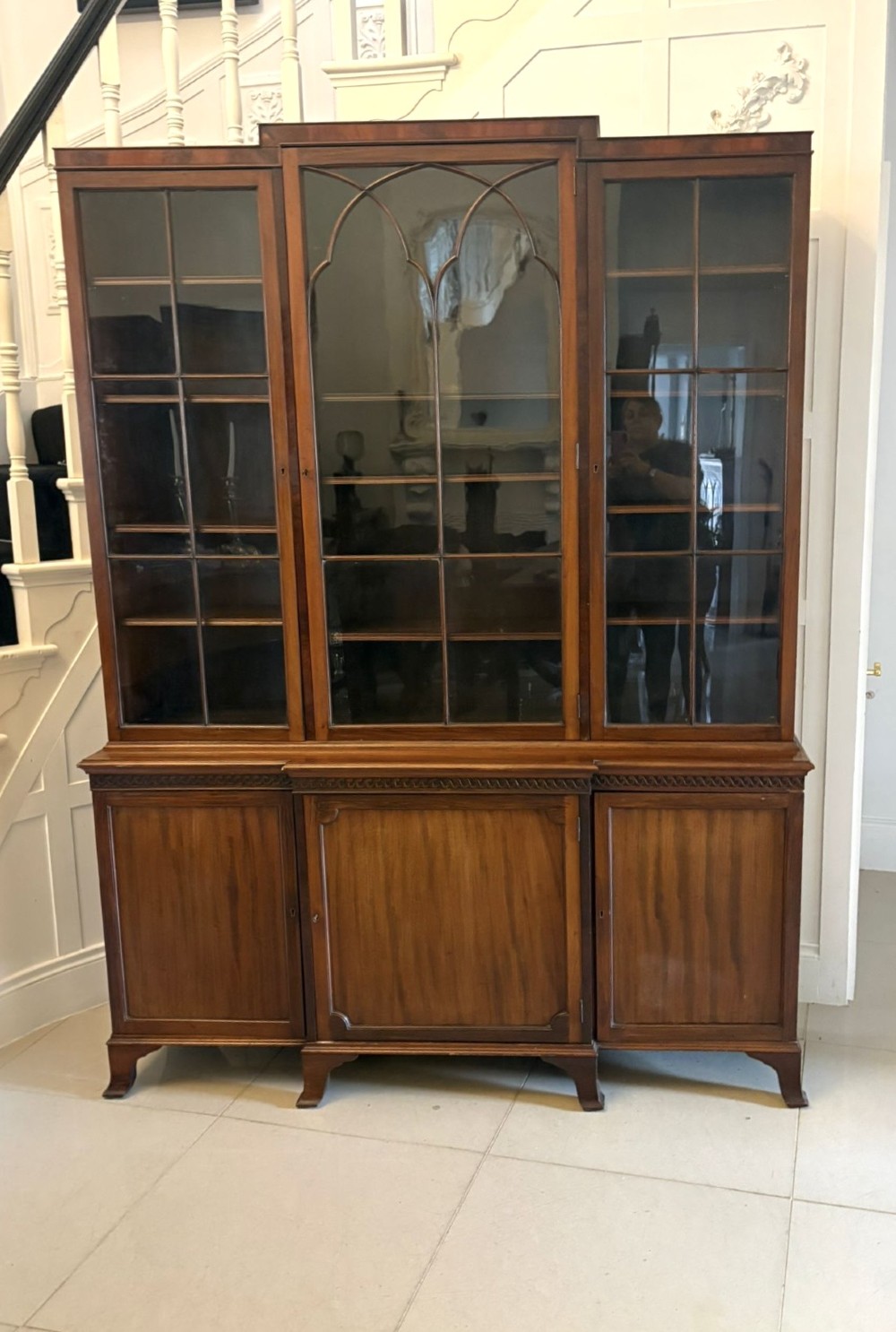 An antique Edwardian mahogany breakfront bookcase featuring three glazed upper doors with astragal moulding above three solid wooden cabinet doors.