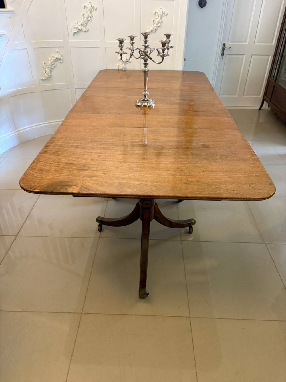A long Regency mahogany extending dining table supported by turned pedestal pillars with splayed legs and brass castors. View II