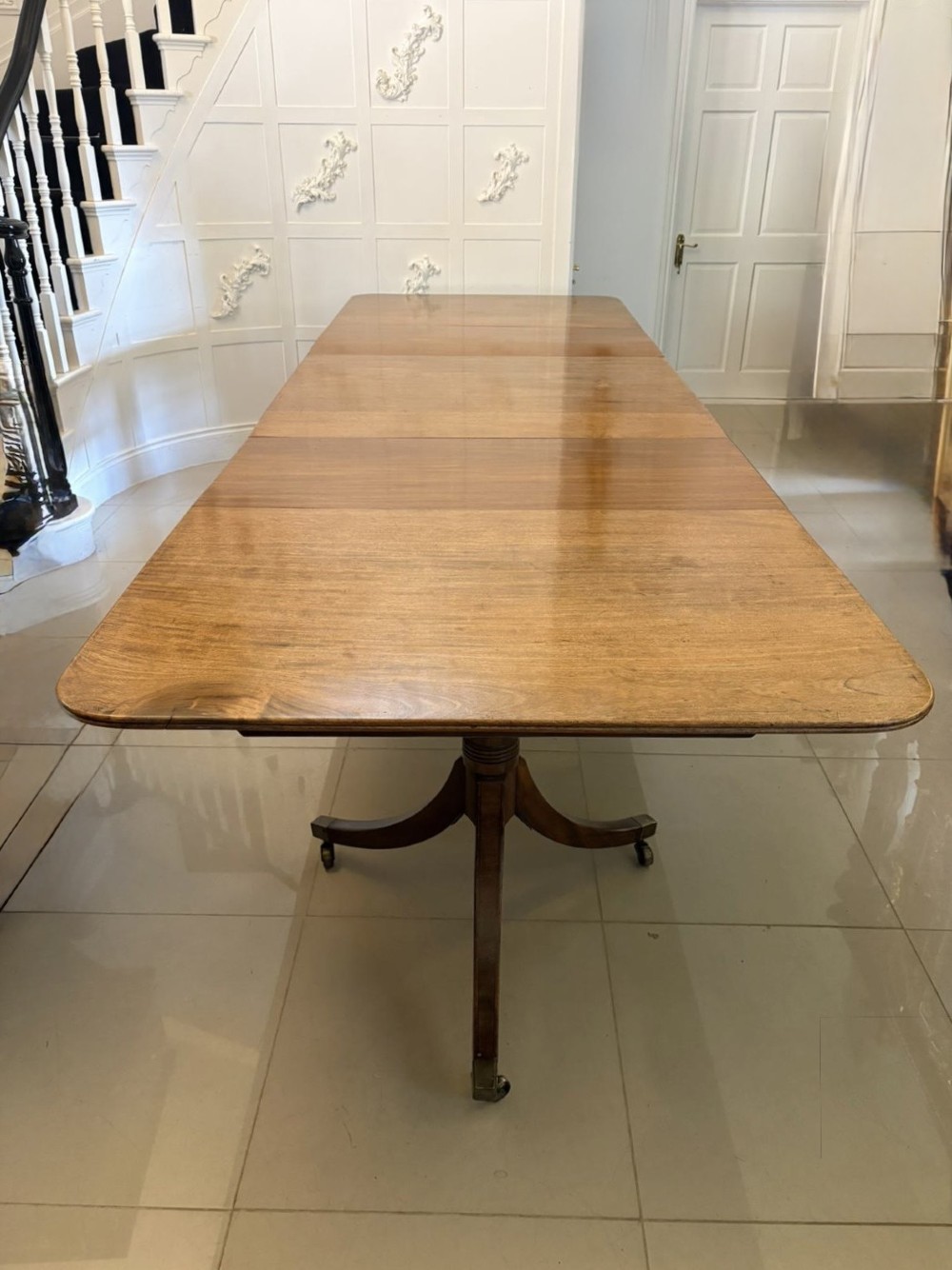 A long Regency mahogany extending dining table supported by turned pedestal pillars with splayed legs and brass castors.