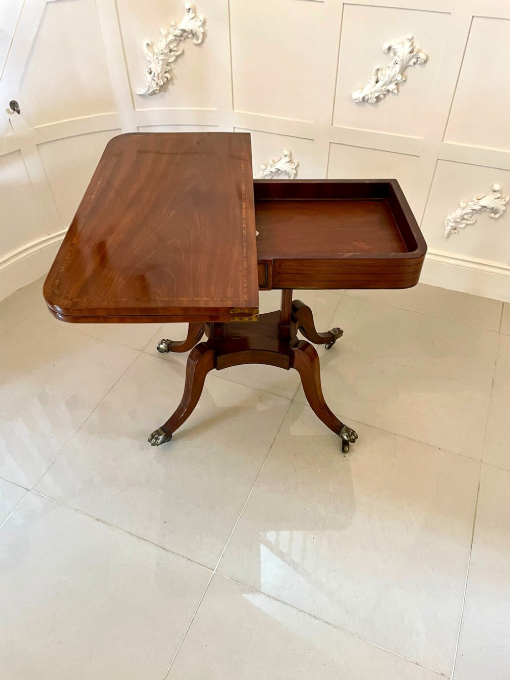 A Regency mahogany fold-over card table featuring an inlaid apron, central pedestal support, and four sabre legs with brass lion paw feet and castors. View IV