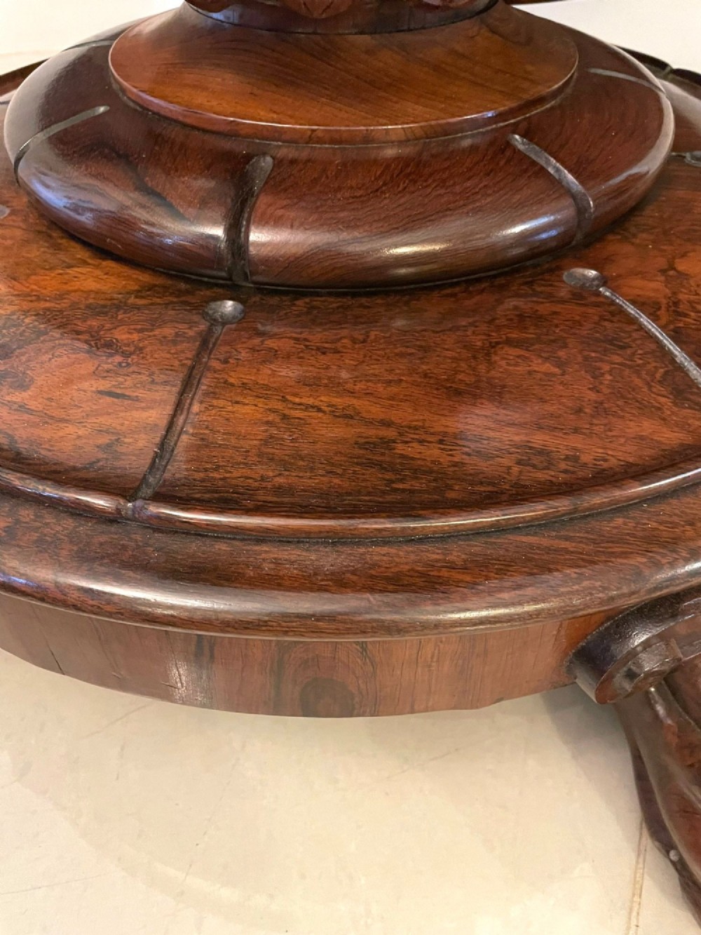 A circular William IV rosewood dining table shown with its top tilted vertically to display the rich wood grain and supported on a carved base with paw feet. View III