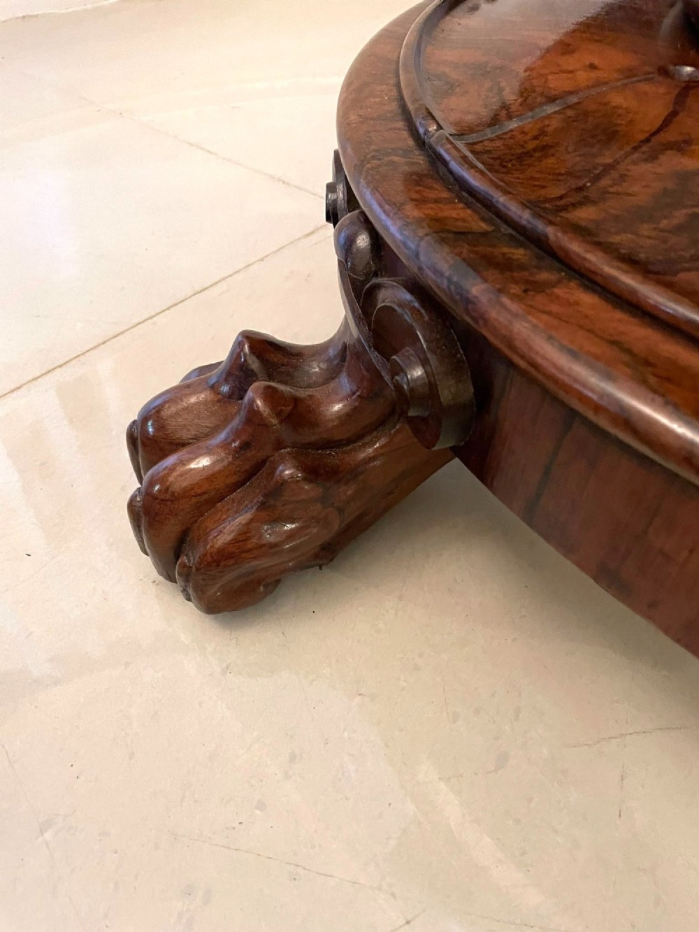 A circular William IV rosewood dining table shown with its top tilted vertically to display the rich wood grain and supported on a carved base with paw feet. View VII