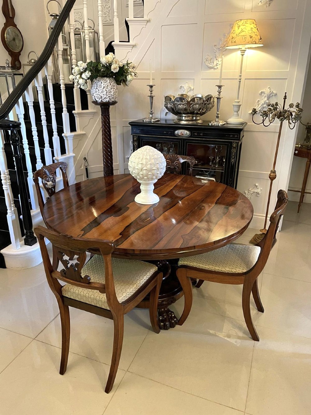 A circular William IV rosewood dining table shown with its top tilted vertically to display the rich wood grain and supported on a carved base with paw feet. View X