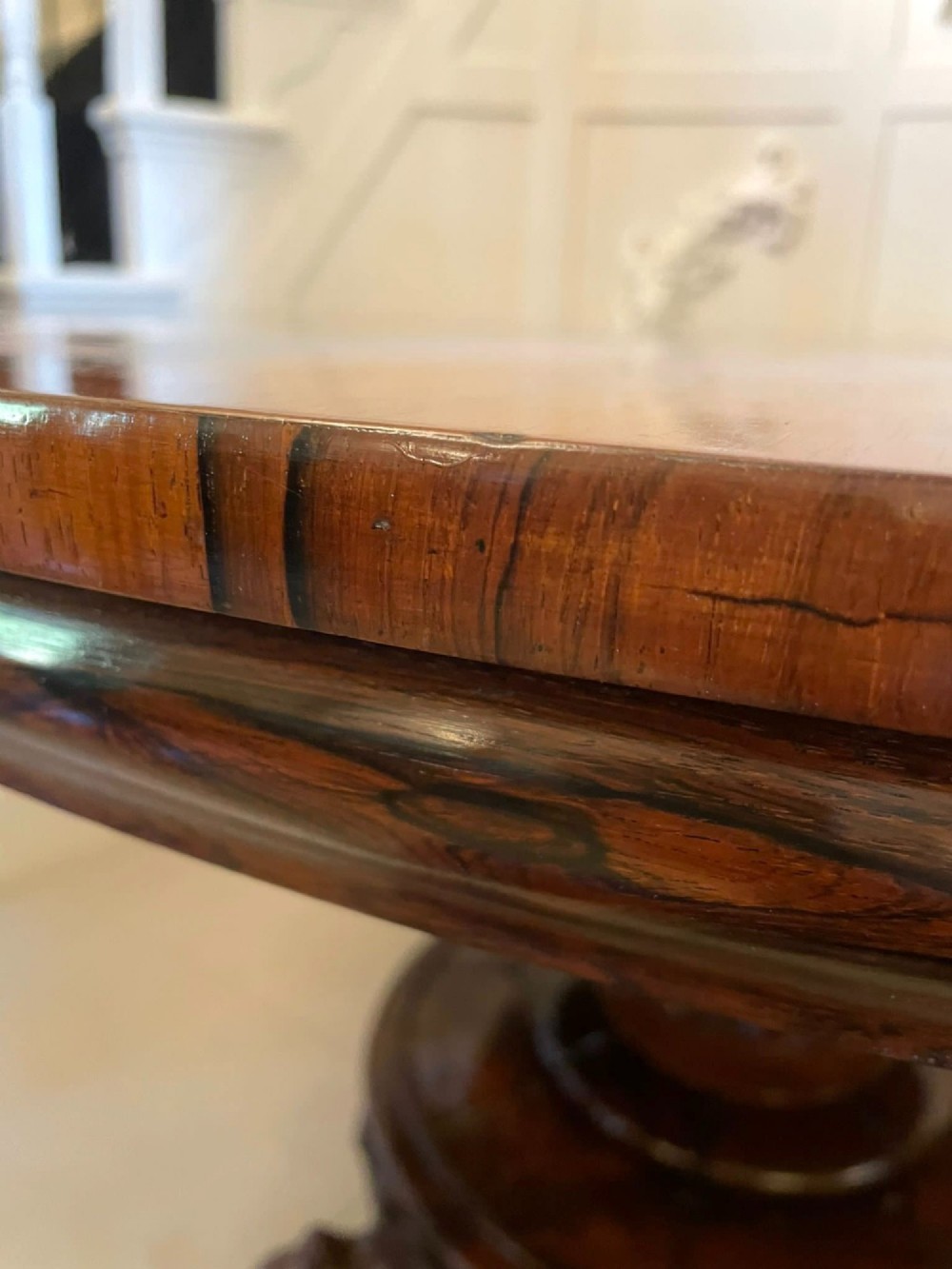 A circular William IV rosewood dining table shown with its top tilted vertically to display the rich wood grain and supported on a carved base with paw feet. View XI