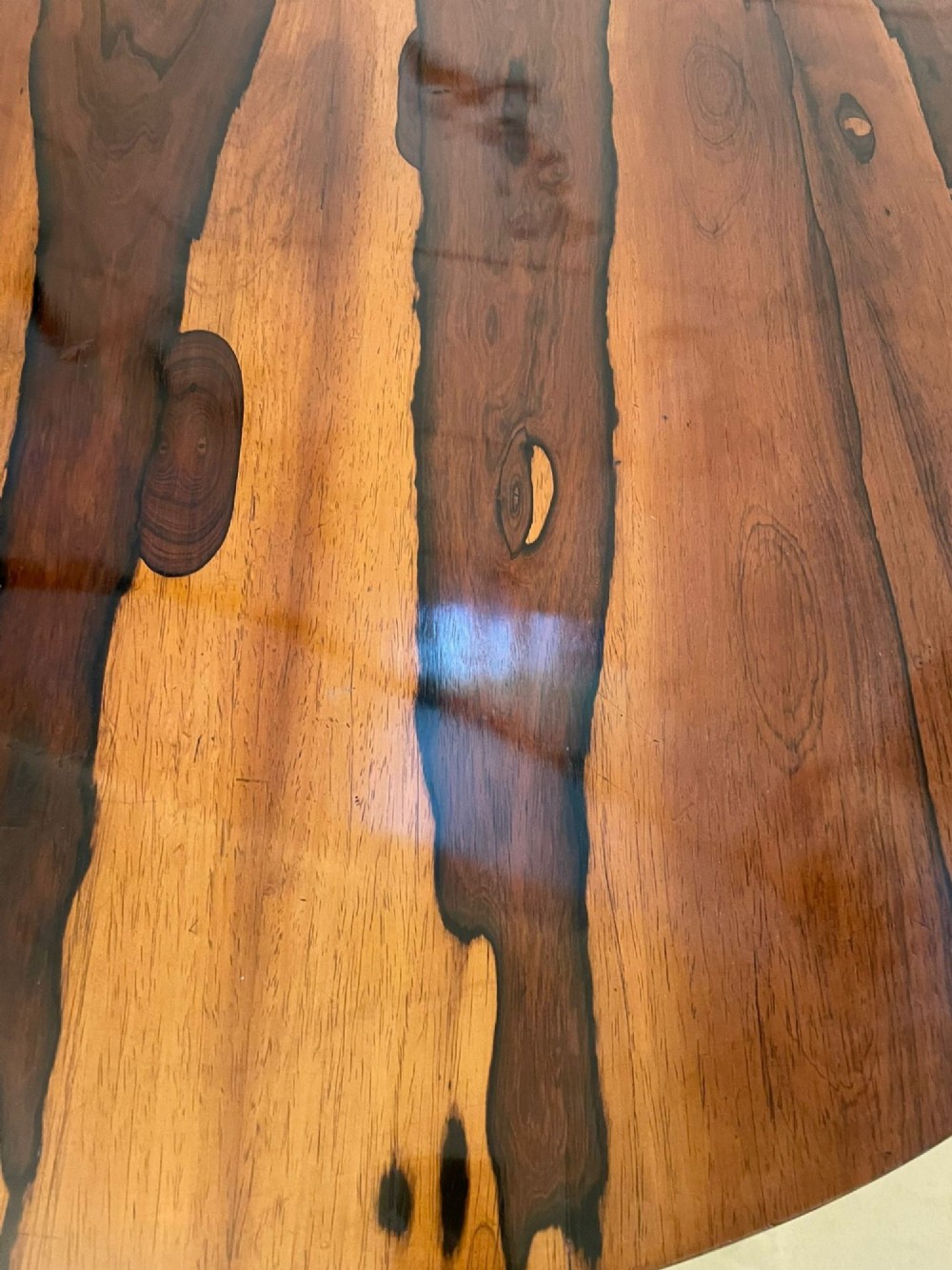 A circular William IV rosewood dining table shown with its top tilted vertically to display the rich wood grain and supported on a carved base with paw feet. View XIII