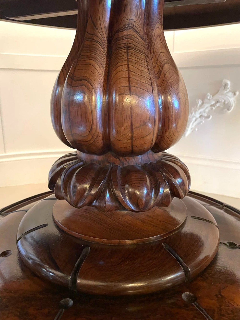 A circular William IV rosewood dining table shown with its top tilted vertically to display the rich wood grain and supported on a carved base with paw feet. View XIV
