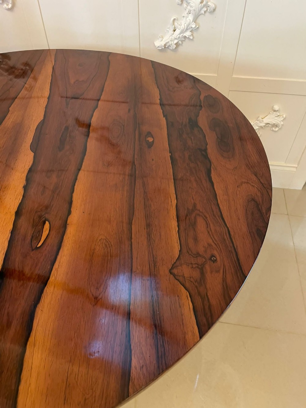 A circular William IV rosewood dining table shown with its top tilted vertically to display the rich wood grain and supported on a carved base with paw feet. View XV
