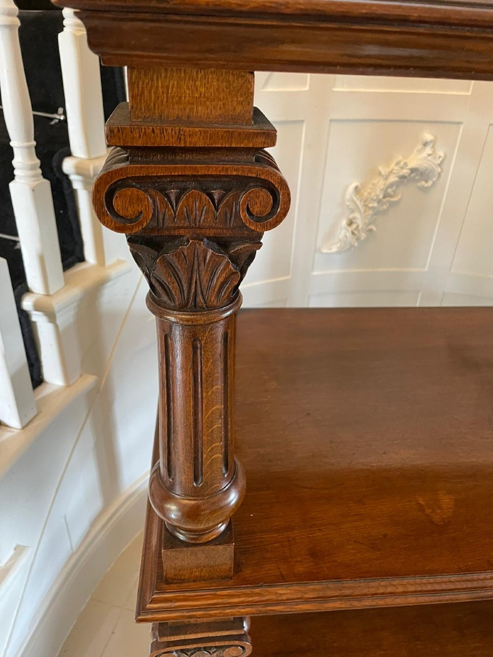 A three-tiered dark oak antique dumbwaiter featuring carved column supports, a carved gallery cresting, and bun feet. View VI