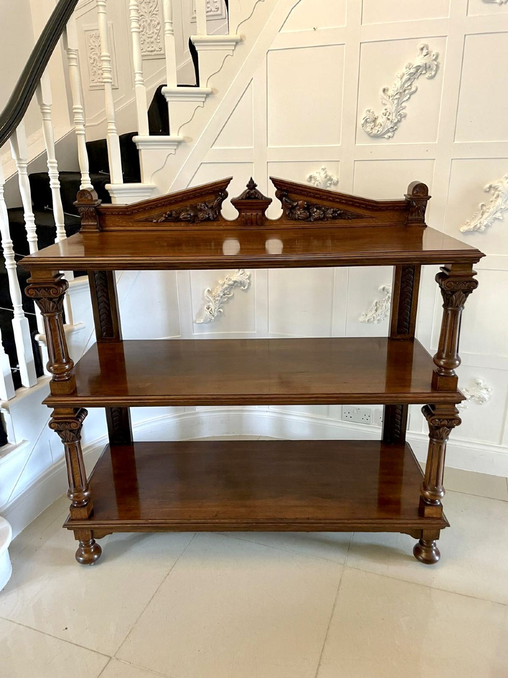 A three-tiered dark oak antique dumbwaiter featuring carved column supports, a carved gallery cresting, and bun feet. View IX