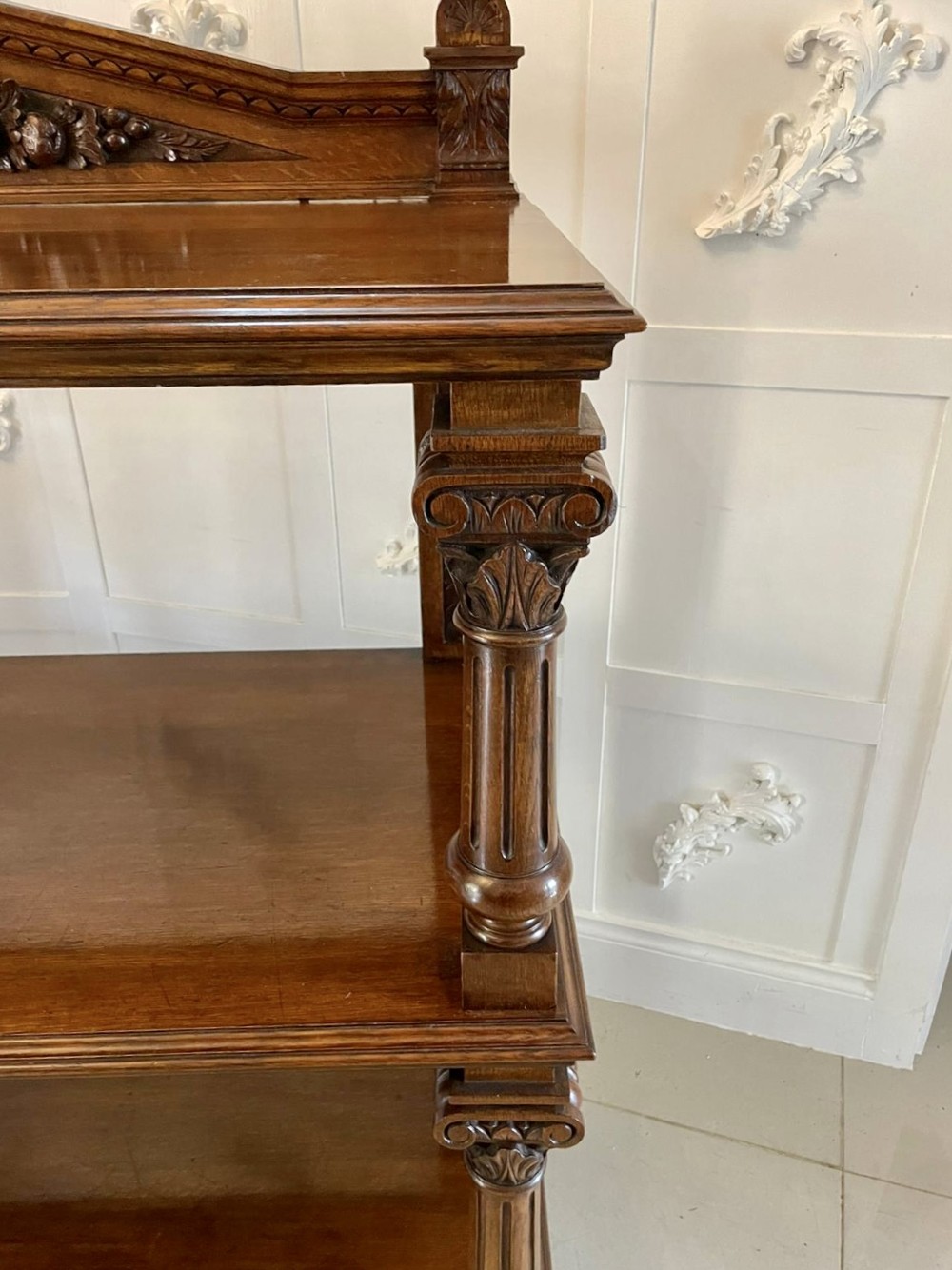 A three-tiered dark oak antique dumbwaiter featuring carved column supports, a carved gallery cresting, and bun feet. View X