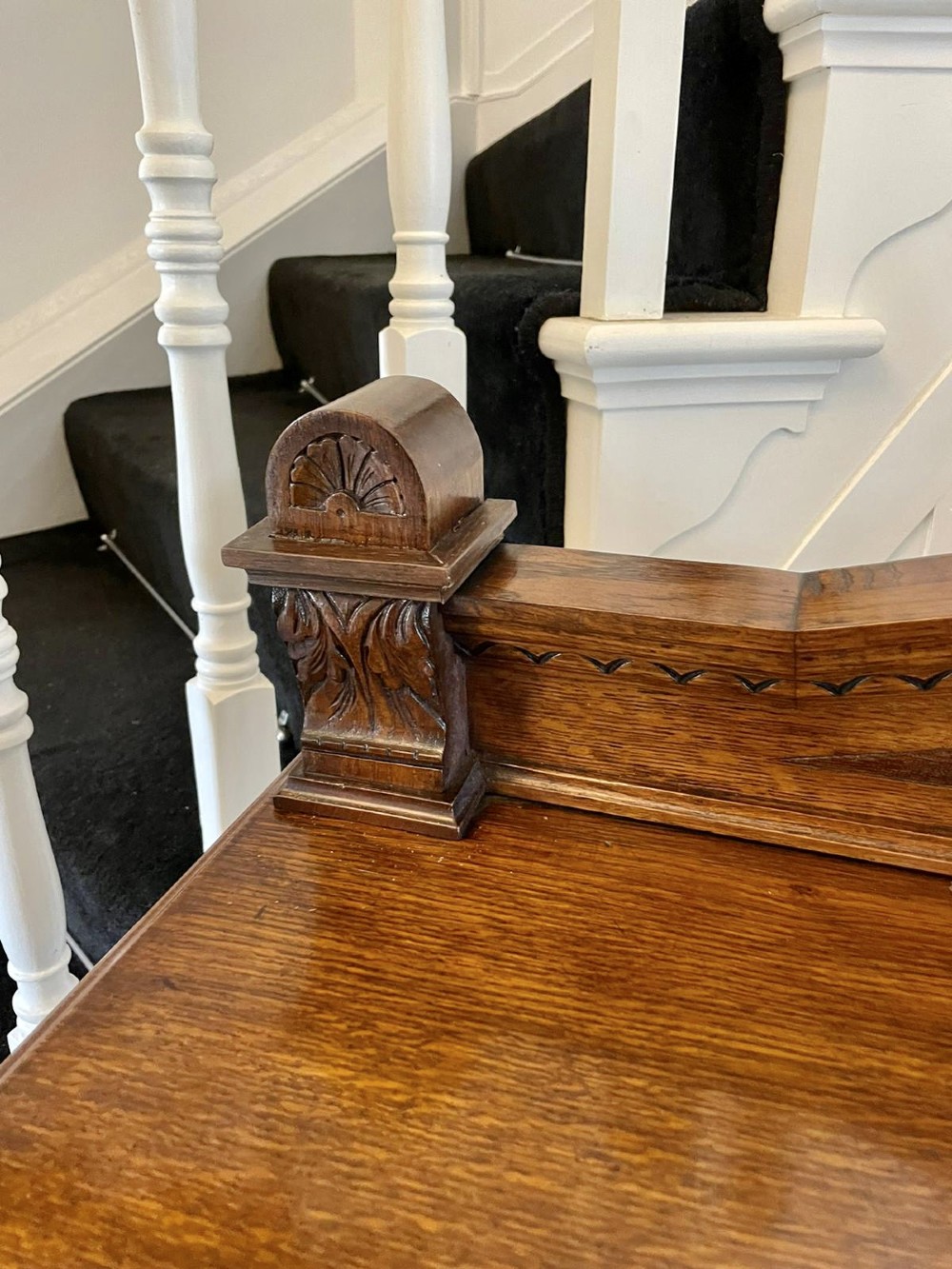 A three-tiered dark oak antique dumbwaiter featuring carved column supports, a carved gallery cresting, and bun feet. View XI