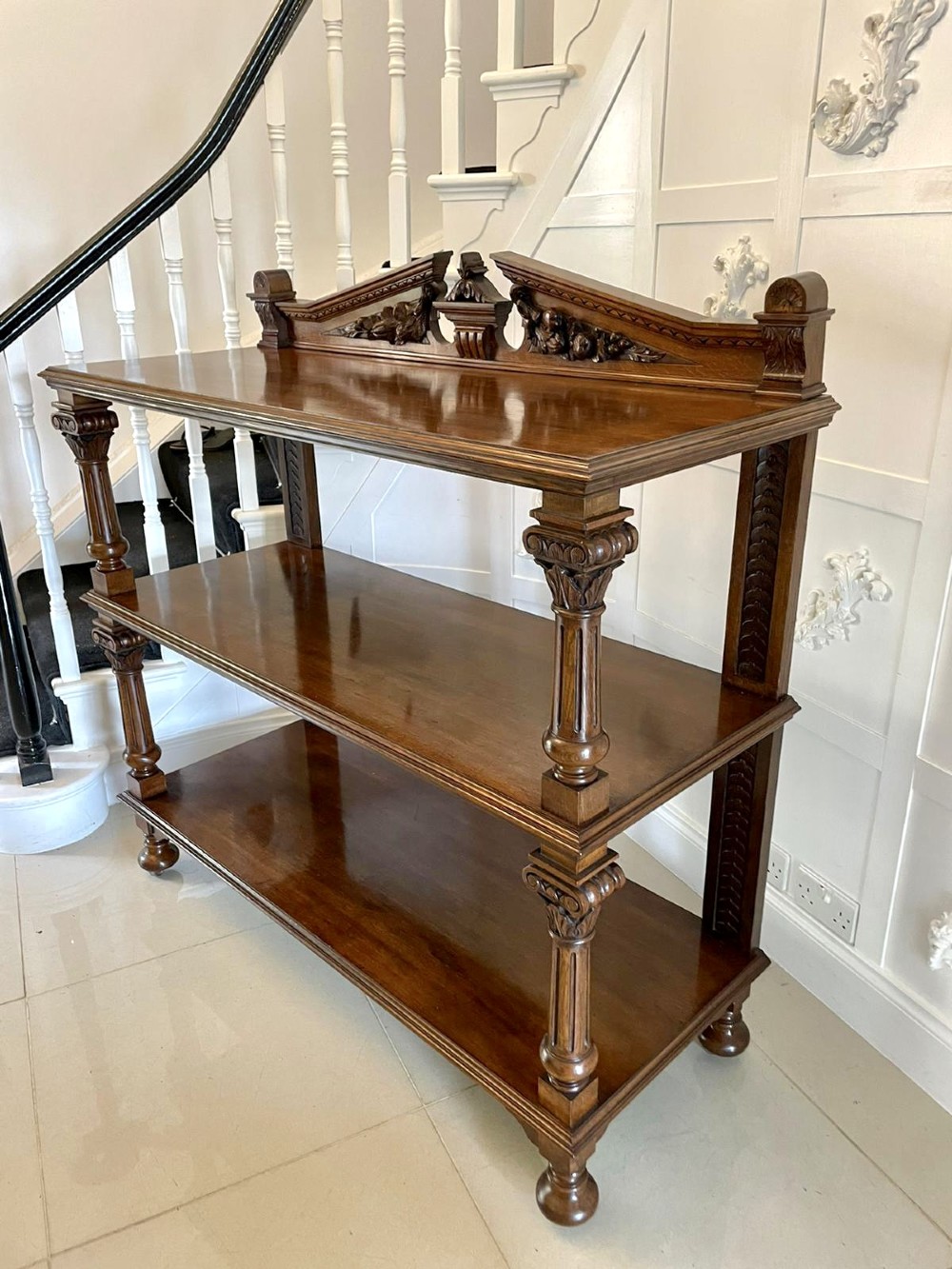 A three-tiered dark oak antique dumbwaiter featuring carved column supports, a carved gallery cresting, and bun feet. View XIII
