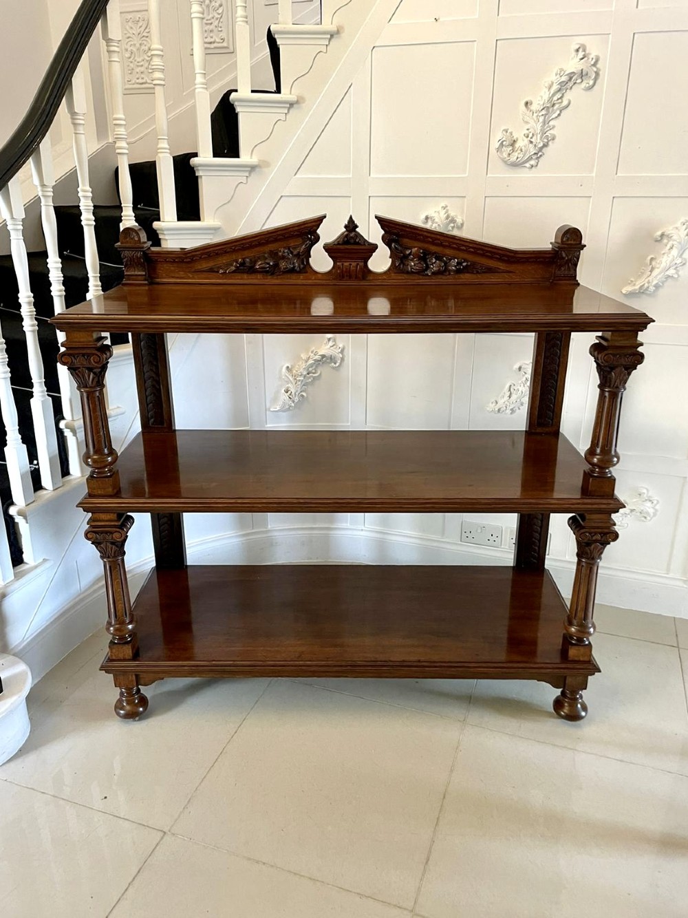 A three-tiered dark oak antique dumbwaiter featuring carved column supports, a carved gallery cresting, and bun feet. View XV