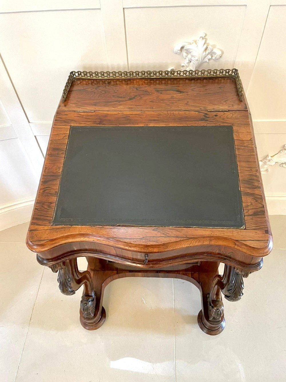 A Victorian rosewood Davenport desk featuring a sloped dark green leather writing surface, decorative brass gallery rail, carved cabriole front supports, and side drawers. View VIII