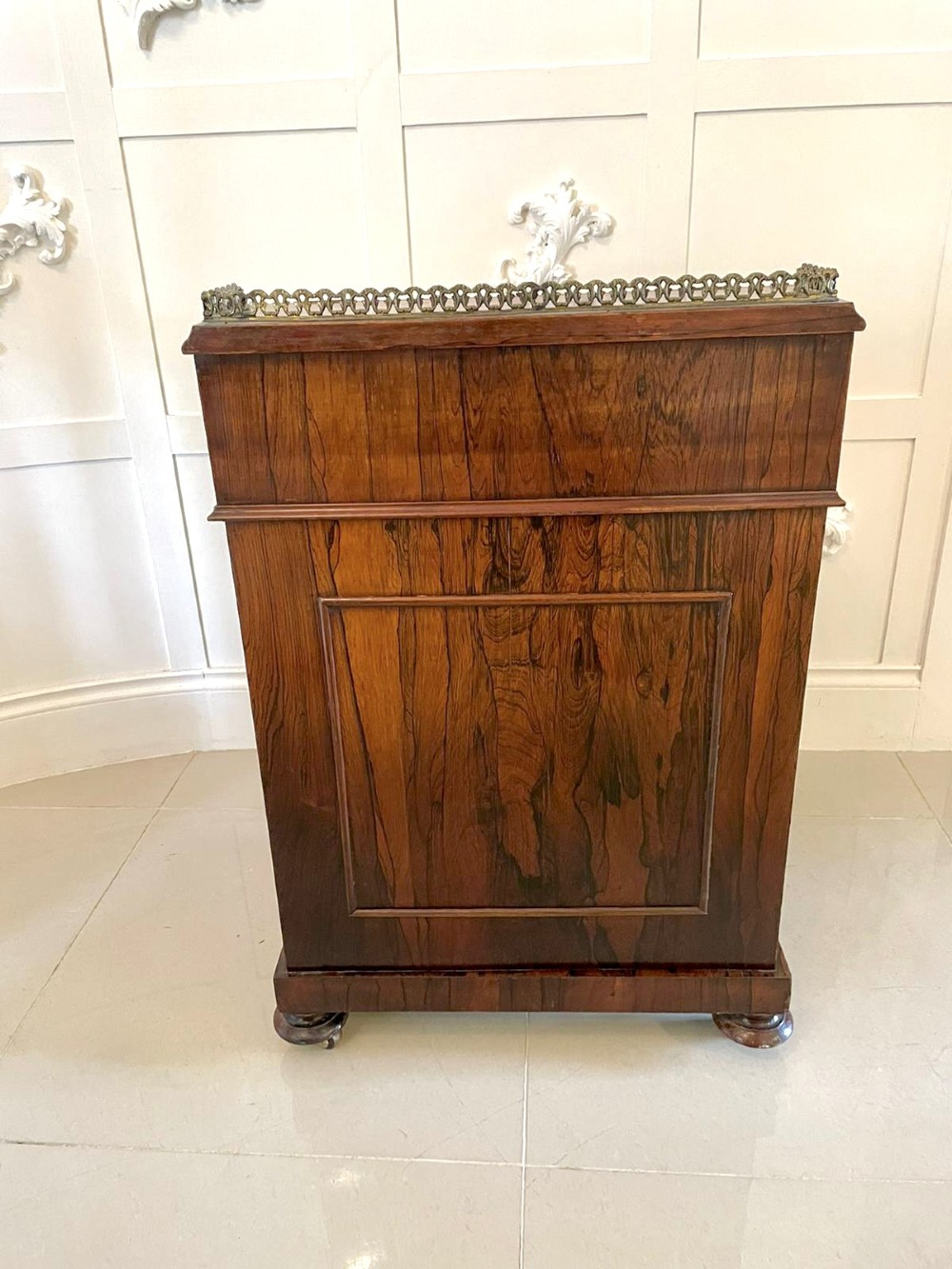 A Victorian rosewood Davenport desk featuring a sloped dark green leather writing surface, decorative brass gallery rail, carved cabriole front supports, and side drawers. View XV