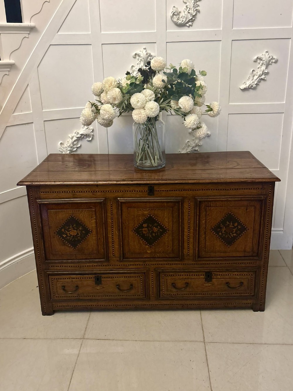 A seventeenth-century oak mule chest with three rectangular panelled sections containing central diamond floral marquetry inlays positioned above two base drawers. View III
