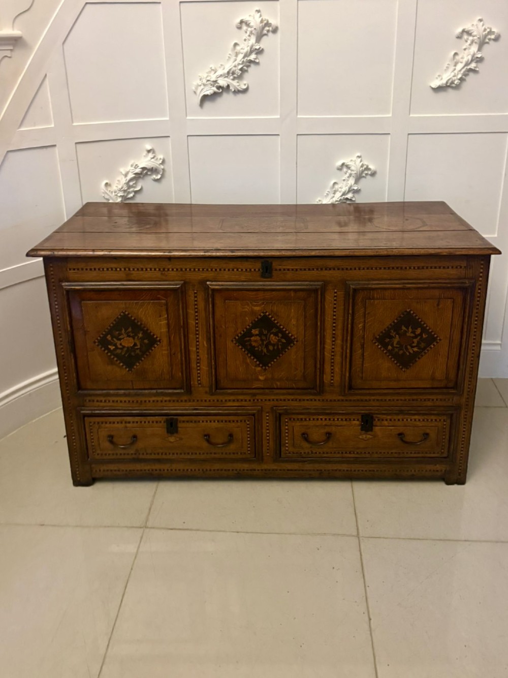 A seventeenth-century oak mule chest with three rectangular panelled sections containing central diamond floral marquetry inlays positioned above two base drawers. View VI