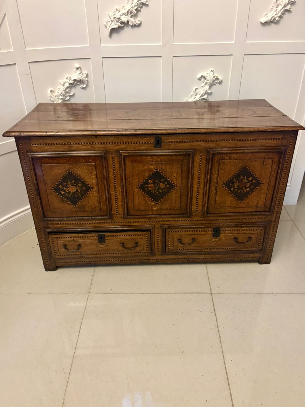 A seventeenth-century oak mule chest with three rectangular panelled sections containing central diamond floral marquetry inlays positioned above two base drawers.