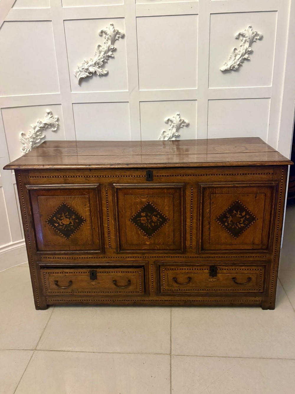 A seventeenth-century oak mule chest with three rectangular panelled sections containing central diamond floral marquetry inlays positioned above two base drawers. View XIV