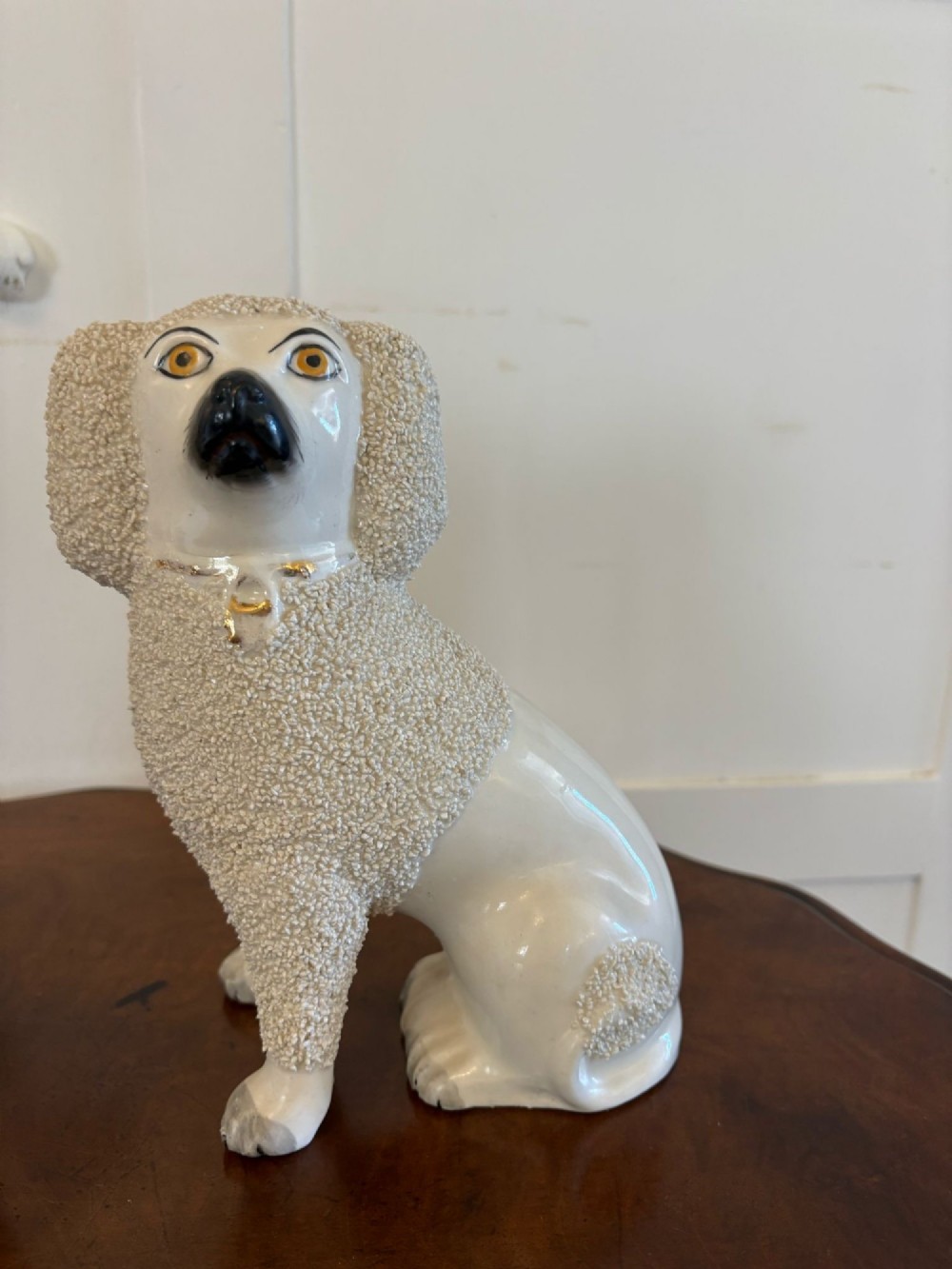 A matching pair of Victorian cream earthenware Staffordshire poodle figurines sitting upright with hand-applied textured fur and gilded collar details. View X