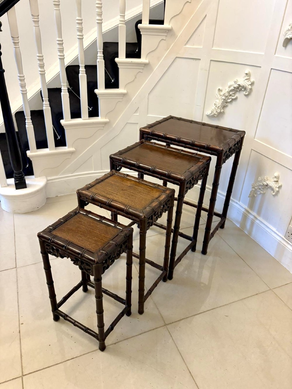 A set of four dark brown carved hardwood nesting tables featuring faux bamboo turnings and openwork carved aprons.