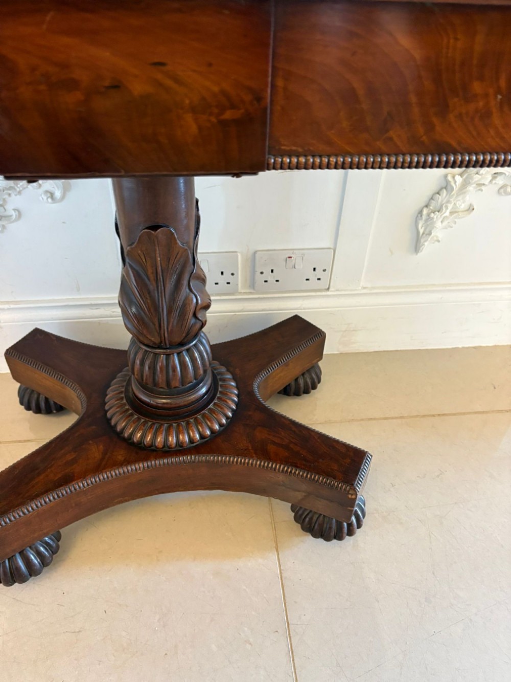 A 19th-century William IV figured mahogany card table with a fold-over top, carved central pedestal, and a concave platform base supported by carved feet. View IV