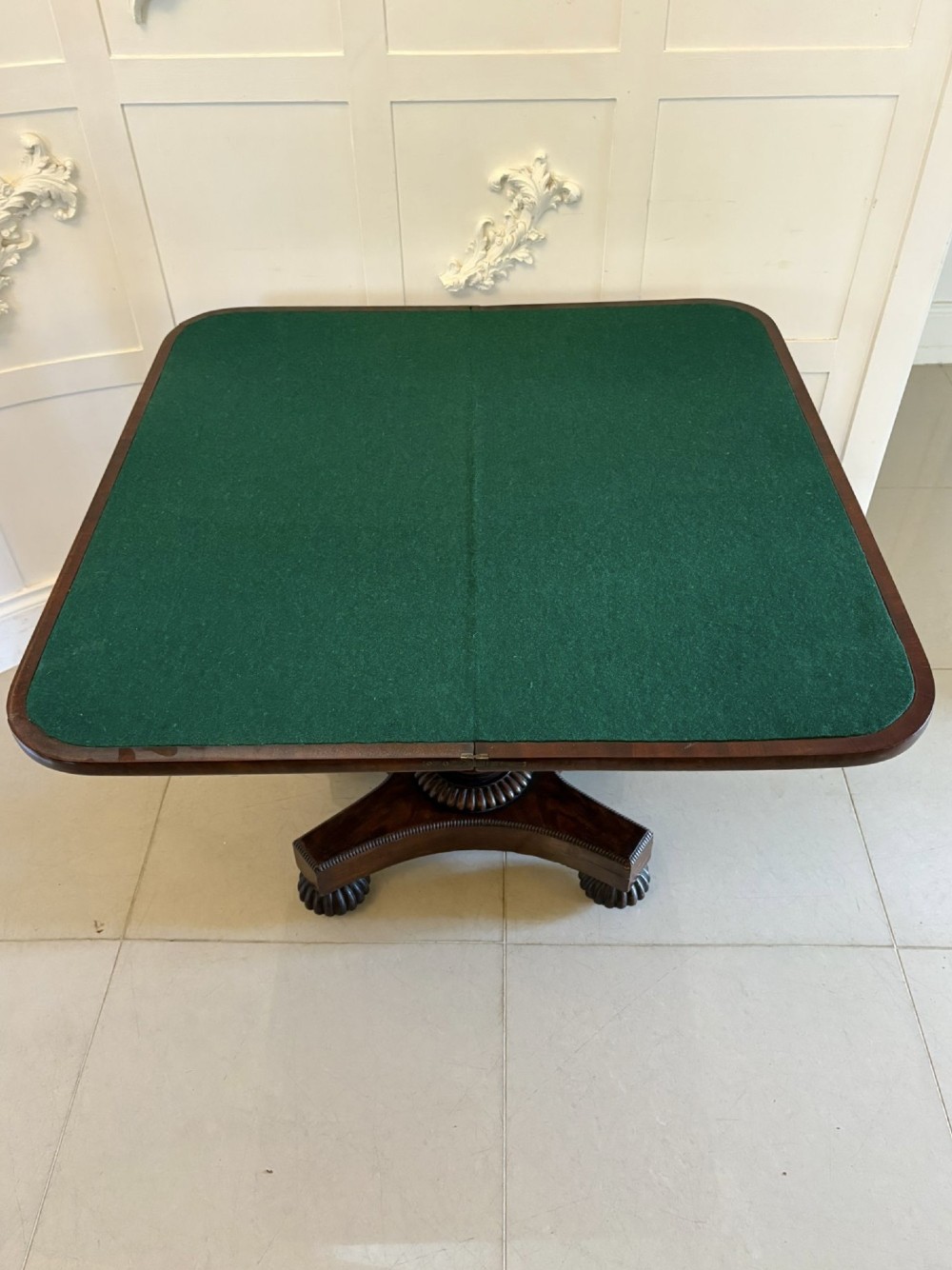 A 19th-century William IV figured mahogany card table with a fold-over top, carved central pedestal, and a concave platform base supported by carved feet. View V