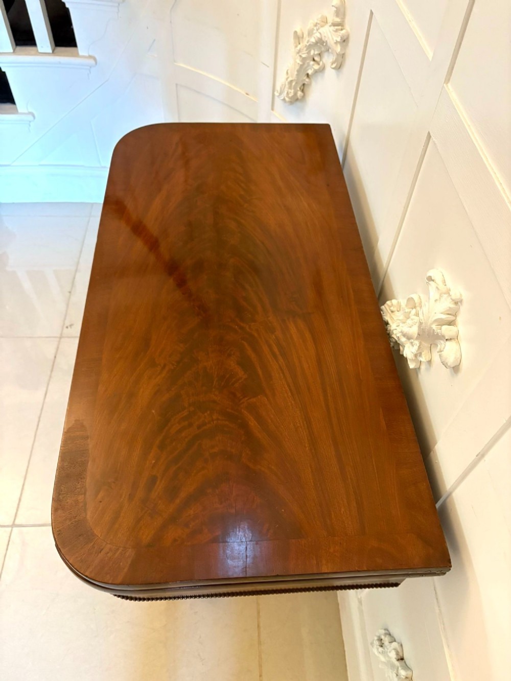 A 19th-century William IV figured mahogany card table with a fold-over top, carved central pedestal, and a concave platform base supported by carved feet. View VIII