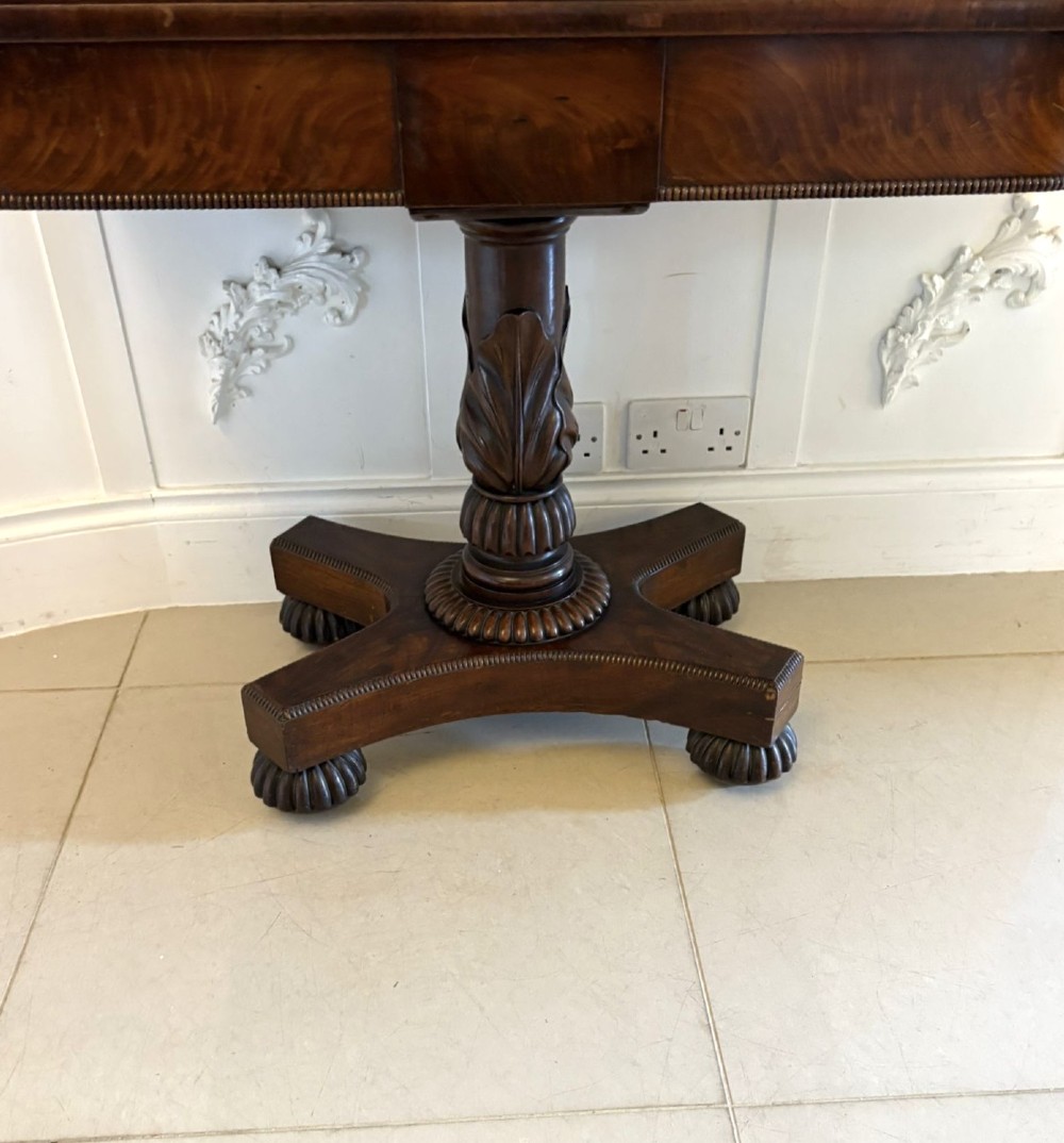 A 19th-century William IV figured mahogany card table with a fold-over top, carved central pedestal, and a concave platform base supported by carved feet. View IX