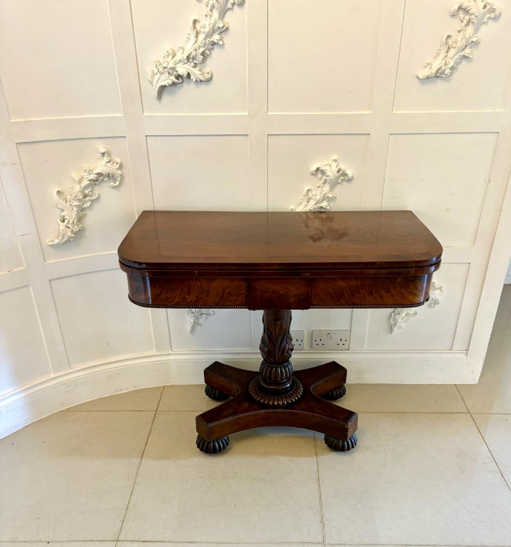 A 19th-century William IV figured mahogany card table with a fold-over top, carved central pedestal, and a concave platform base supported by carved feet. View XI