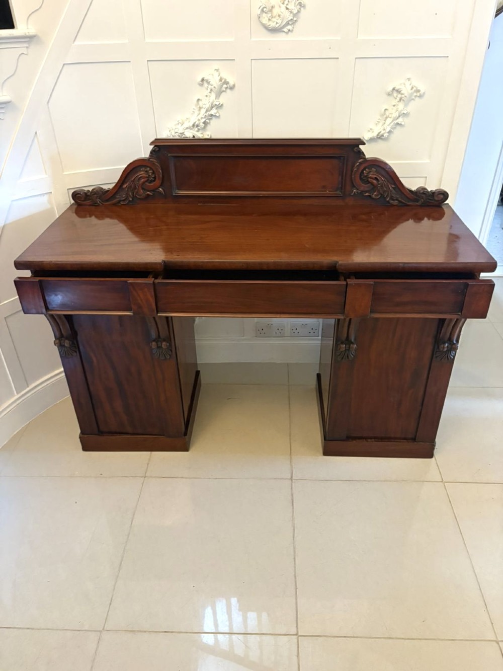 A Victorian mahogany pedestal sideboard featuring a raised backboard with carved scrollwork and two flanking pedestal cupboards. View V