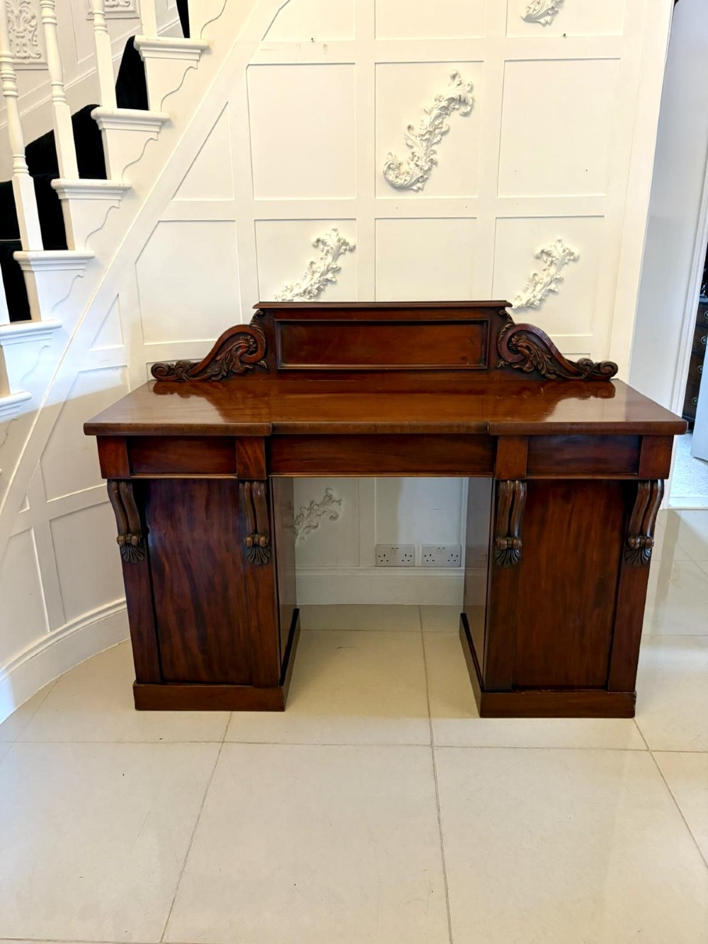 A Victorian mahogany pedestal sideboard featuring a raised backboard with carved scrollwork and two flanking pedestal cupboards.