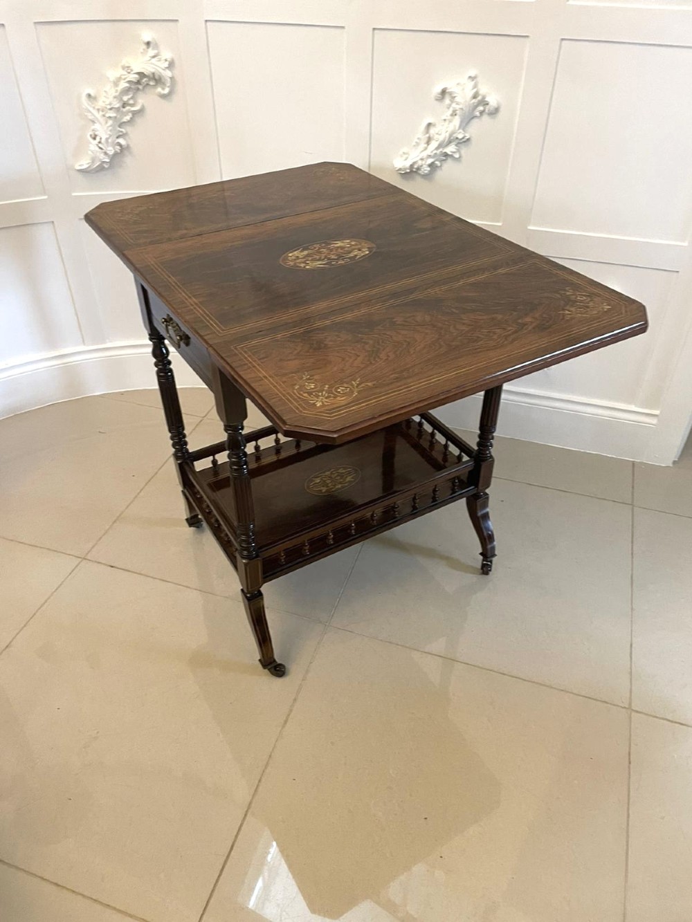 A Victorian rosewood drop-leaf centre table featuring floral marquetry inlay, turned legs on brass castors, and a lower tiered shelf with a spindle gallery. View V